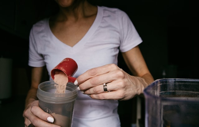 A women adding a scoop of whey protein to her protein shake. Whey protein is one of the most important bodybuilding supplement in this list.